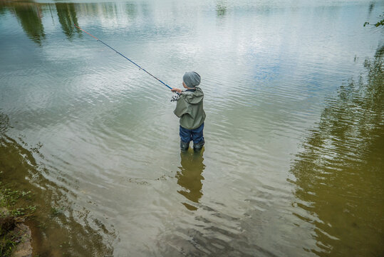 Boy Catching Fish Standing In Water In Big Boots