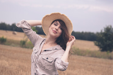 A young attractive girl in a straw hat stands in a field.