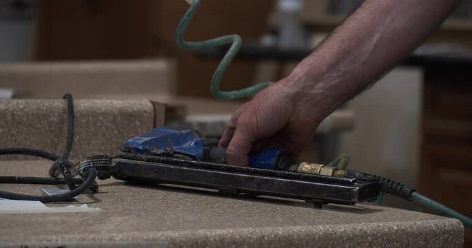 Slow motion shot of a tradesman picking up an air powered staple gun in a workshop. Close up.
