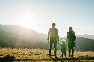 Family with kid hiking in mountains. Young tourists on top of a mountain enjoying valley view...