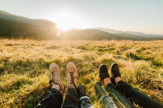 Legs of traveler family with child sitting on a high mountain. Close Up. People enjoying the sunset in mountains. The concept of family travel, adventure, and tourism. Hiking autumn vacations outdoor.