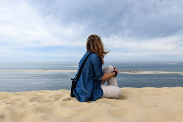 A blonde woman sitting on her back in the area with the blue sea in the background

