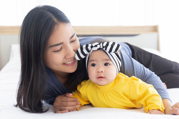 An Asian mom plays with her baby in bed with love and care.