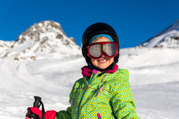 Active adorable preschooler caucasian smiling kid girl portrait with ski in helmet, goggles and bright suit enjoy winter sport activities . Little child skiing on luxury alpine resort in mountains