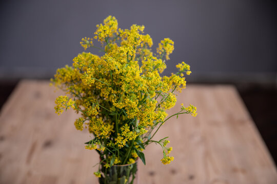 Bunch of dandelions and canola in glass vase on wooden table, yellow flowers' bouquet
