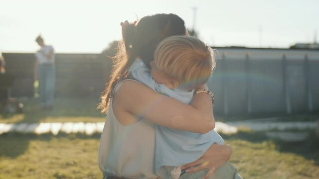 Happy young mother hugging and kissing adorable little son in the backyard on sunny summer day