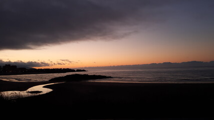 Fototapeta premium Atardecer en las costas gallegas desde el pueblo de San Cosme De Barreiros. se aprecian las ultimas luces sobre la arena, el agua y el arroyo que desemboca en el mar