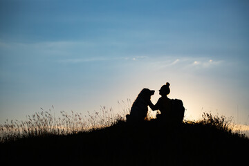 Fototapeta na wymiar Woman with her dog sitting on the hill in the sunset.