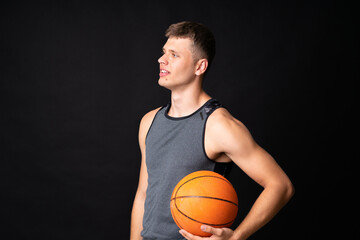 Handsome young man playing basketball over isolated black wall