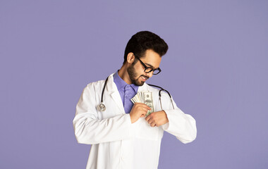 Corruption in healthcare concept. Indian doctor putting money into his pocket on lilac background