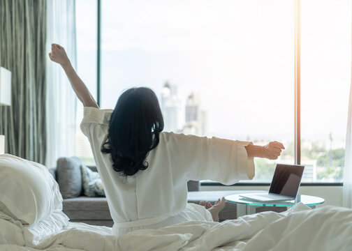 Work-Life balance and life quality concept with woman rear view in rest relaxing on bed, take it easy in modern hotel guest room or luxury home living room with beautiful business city urban scene