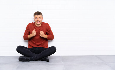 Young handsome man sitting on the floor celebrating a victory