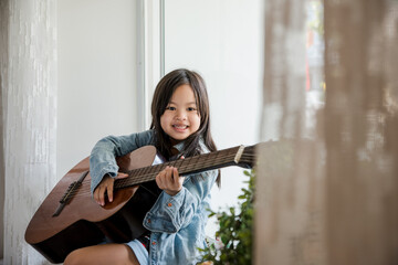 Girl play guitar at home window light 