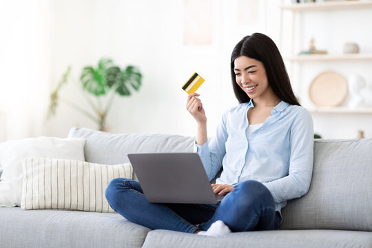 Joyful asian woman using laptop and credit card at home, buying online