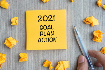 2021 Goal, Plan, Action word on yellow note with Businessman holding pen and crumbled paper on wooden table background. New Year New Start, Resolutions, Strategy  concept