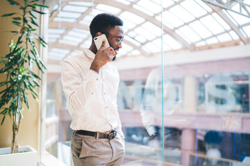 Elegant black man speaking on smartphone standing at window in shopping center