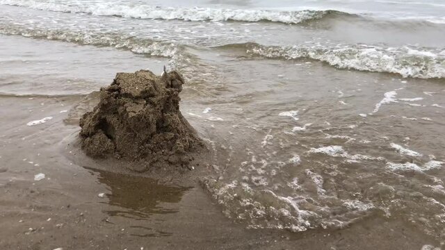 A sand castle is slowly washd away by the sea