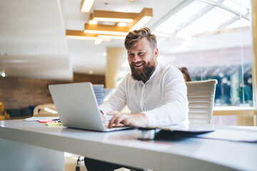 Cheerful businessman typing on laptop in modern workspace