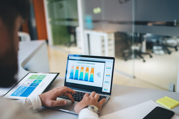 Cropped image of male typing on laptop computer creating online finance report about business income, man's hands on keyboard making research and graphic diagrams for statistic revenue 