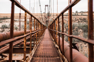 Old iron non-functioning suspension bridge over a dried river side view. Old pedestrian bridge in Moldova. 