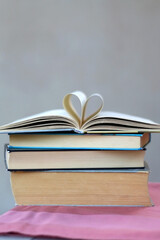 Stack of hardcover books. Top book has pages folded in a heart shape. Selective focus, grey background.