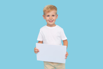 A cute laughing child boy is holding a white signboard with an empty space for text. Advertising of childrens products and the announcement of discounts and sales