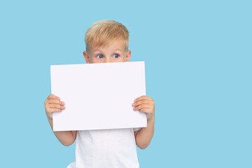 A cute laughing child boy is holding a white signboard with an empty space for text. Advertising of childrens products and the announcement of discounts and sales