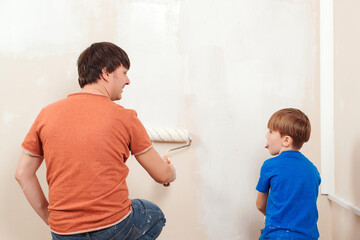 Fototapeta premium Happy family renovating their new home. Father showing his son how painting wall with a roller.