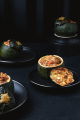 Round zucchini stuffed with meat, tomatoes and parmesan on dark plates. Dark background.