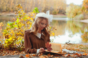 Portrait of young woman in retro dress reading a book in autumn park