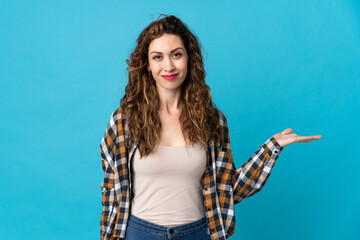 Young caucasian woman isolated on blue background holding copyspace imaginary on the palm to insert...