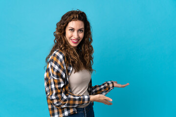 Young caucasian woman isolated on blue background extending hands to the side for inviting to come