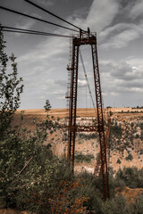 Old iron non-functioning suspension bridge over a dried river side view. Old pedestrian bridge in Moldova.