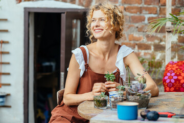 Women's hobby. Female nerd florist make a mini terrarium with house plants. Blond haired woman gardener in brown overalls planting succulents outdoor in cosy terrace or backyard.