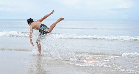 Asian man is learning to ride a skim board or surf board and is suddenly lost balancing and body position. (selective focus)