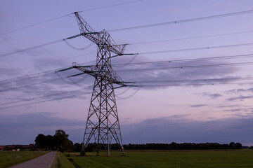 Farmland field with silhouette of electricity tower construction and power lines against a colourful magenta blue purple sunset sky