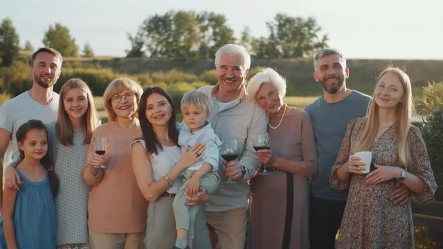 Large Caucasian family standing together outdoors, posing for camera and smiling while gathering together on summer weekend