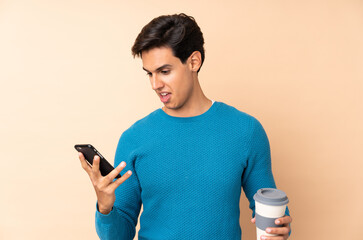Man over isolated background holding coffee to take away and a mobile