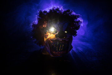 Spooky Clown head on wooden table. Evil clown head smiling on dark foggy background. Halloween...
