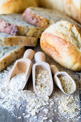 Close up of wooden scoops with flour, oats and oat bran surrounded by various bread.