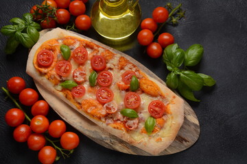 Flatbread pizza garnished with fresh cherry tomatoes,basil,cheese and olive oil on wooden pizza board. Dark background