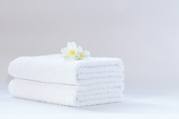 Obraz na płótnie Canvas Two white neatly folded terry towels with a jasmine flower on a light background.