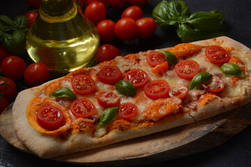 Flatbread pizza garnished with fresh cherry tomatoes,basil,cheese and olive oil on wooden pizza board. Dark background