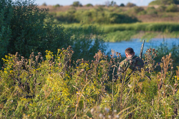 Obraz na płótnie Canvas Hunting season concept. Rural landscape with one hunter near the pond, back view