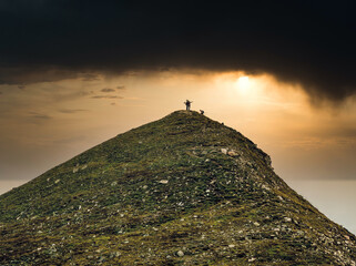 Dramatic landscape with three hikers reaching the top of the mountain. Pyramid shaped mountain peak in Bucegi Mountains.