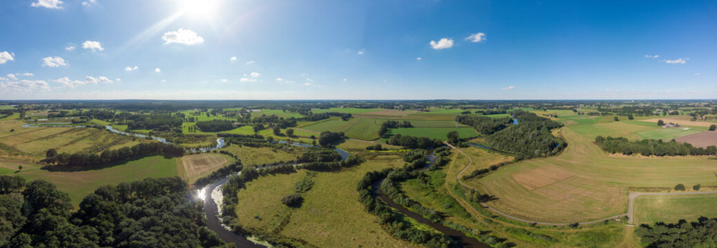 Super wide aerial panorama of the river Regge meandering through the green Dutch Twente farmland landscape against a blue sky and clouds