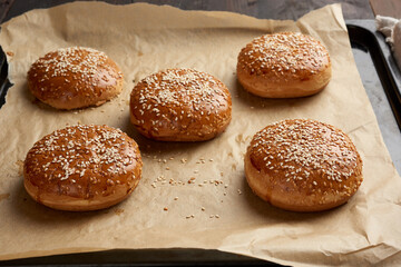 baked sesame buns on brown parchment paper, ingredient for a hamburger