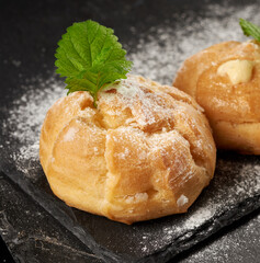 baked custard eclairs and sprinkled with powdered sugar and decorated with a mint leaf on a black board