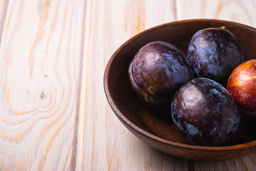 Fresh sweet plum fruits in brown wooden bowl, wood table background, angle view macro