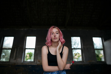 Young funky teenage girl with pink hair holding lollipop candy in abandoned building.